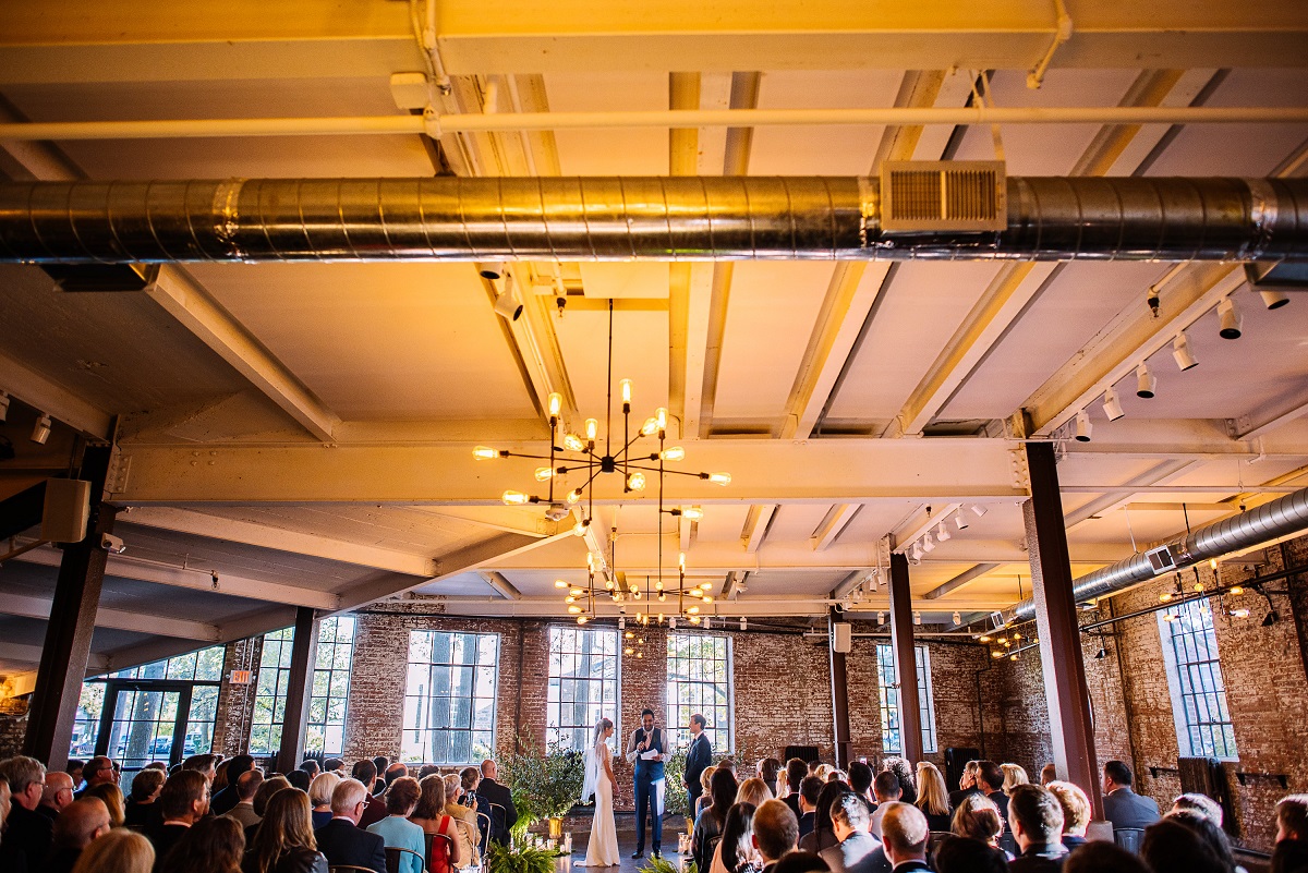 wide shot of an indoor wedding, featuring the bride and groom exchanging vows